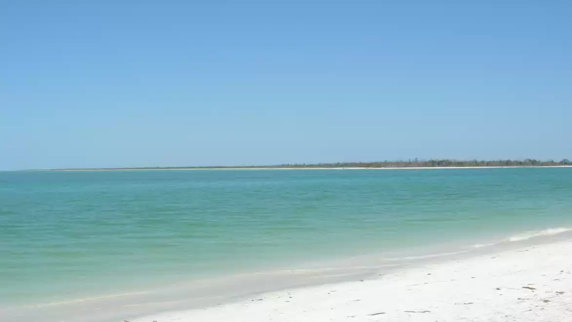 A tranquil white sandy beach with turquoise water and a clear blue sky in the background.