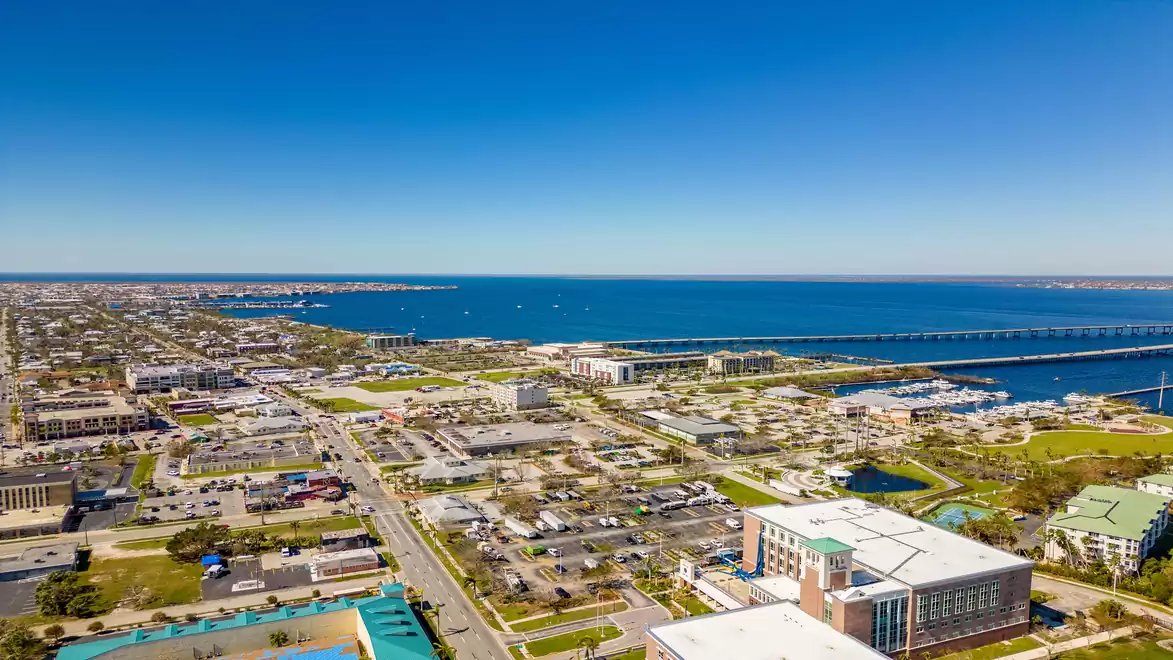 Aerial view of a coastal city with a blue sky and a large body of water on the horizon.