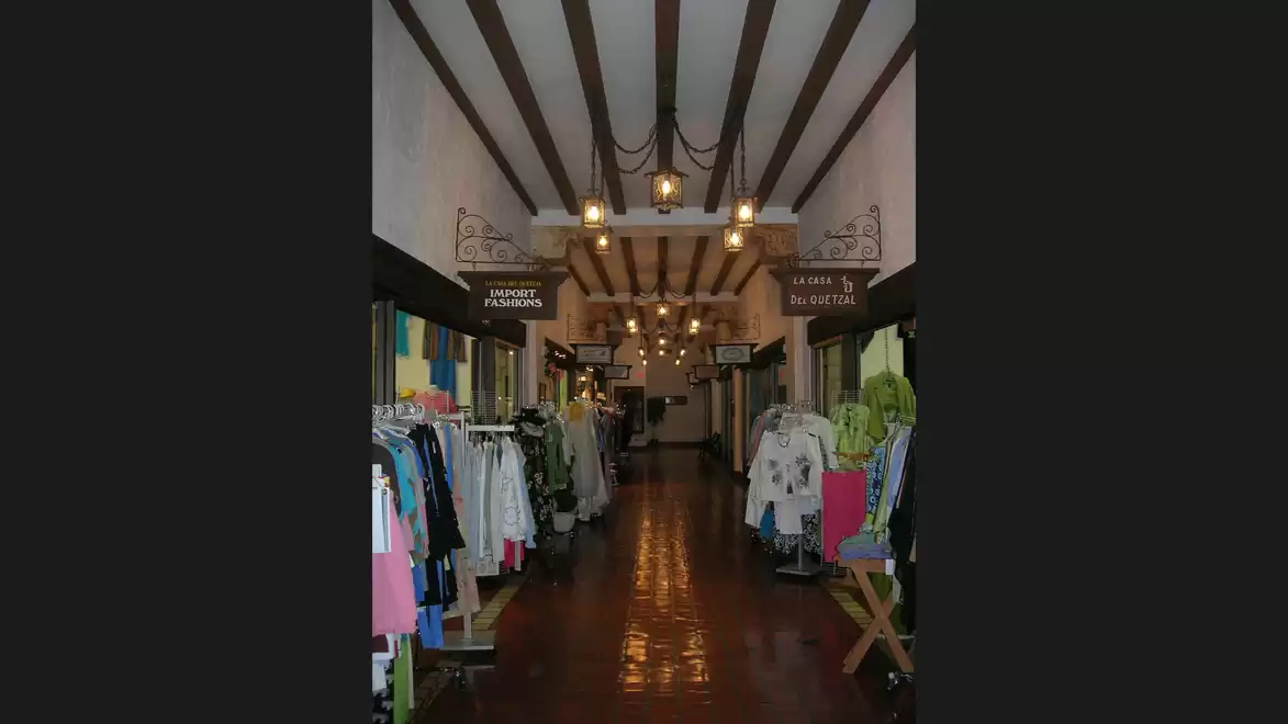 A hallway in a clothing store with a wooden ceiling and clothing racks on both sides.