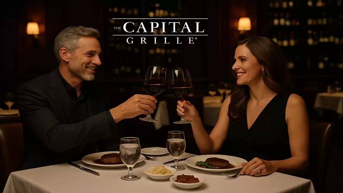 A couple in elegant evening attire toasts in a stylish restaurant. The table is set with a fine dinner.