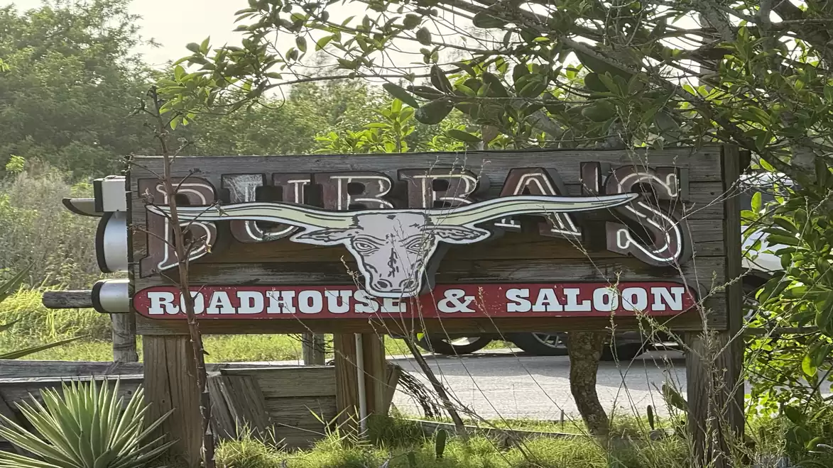 A wooden sign of Bubba's Roadhouse & Saloon featuring a longhorn design surrounded by greenery.