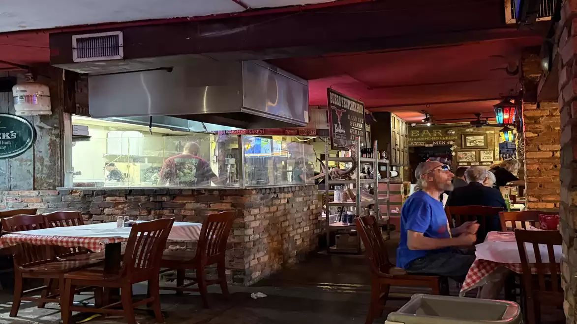 Cozy restaurant with brick walls and checkered tablecloths. Guests are sitting and enjoying their meals.