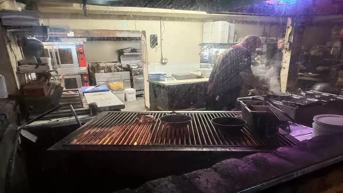 A busy restaurant kitchen with a chef working over a hot grill and steam.