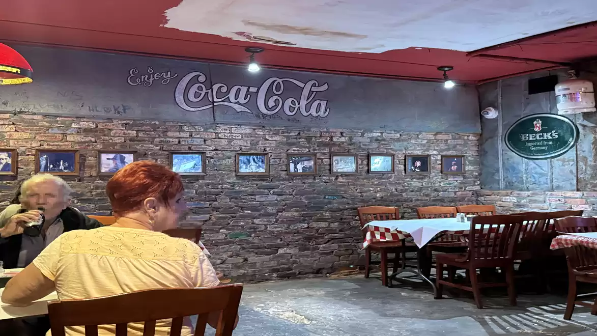 Interior view of a rustic café with Coca-Cola advertisement on a brick wall. Two people sitting at a table enjoying their drink.