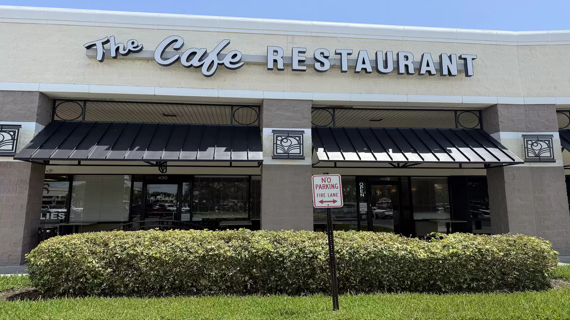 Exterior view of a cafe and restaurant with large windows and a sign reading 'The Cafe Restaurant'.