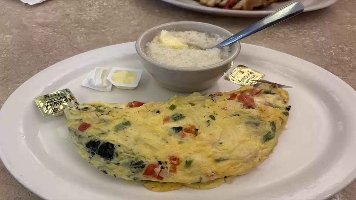 A plate with a vegetable omelette, a bowl of butter, and three small butter packets.