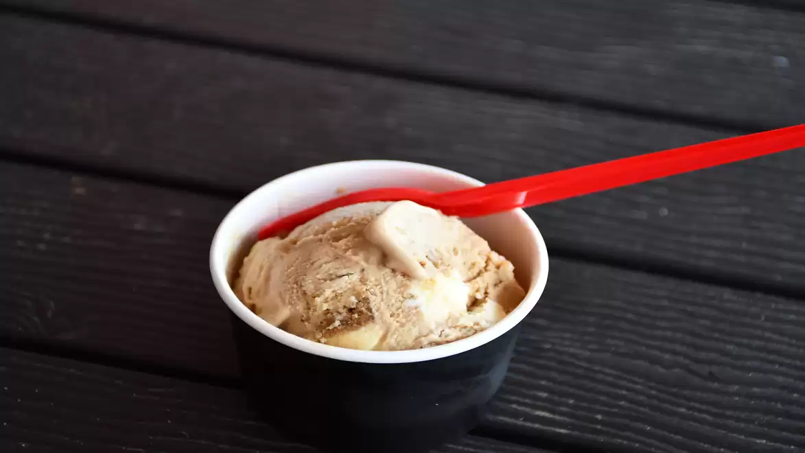 A serving of chocolate ice cream in a black cup with a red spoon on a dark wooden table.