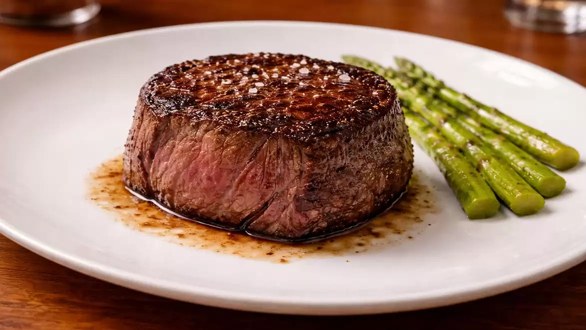 A juicy filet steak served on a white plate with green asparagus spears as a side.