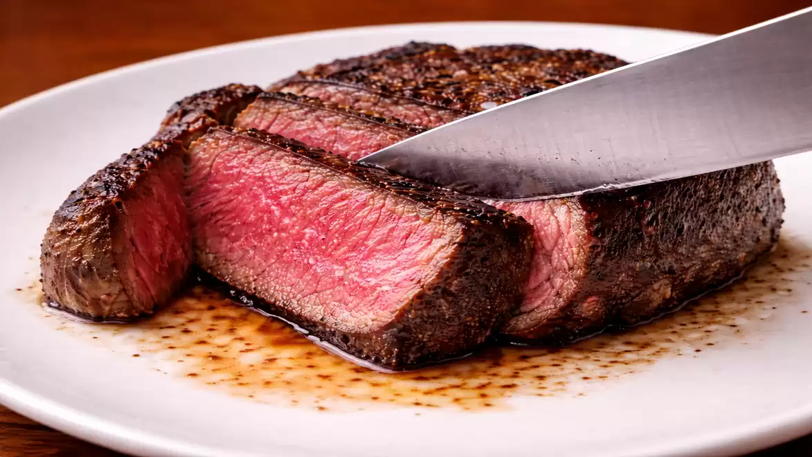 Close-up of a perfectly cooked, juicy steak being sliced on a white plate.