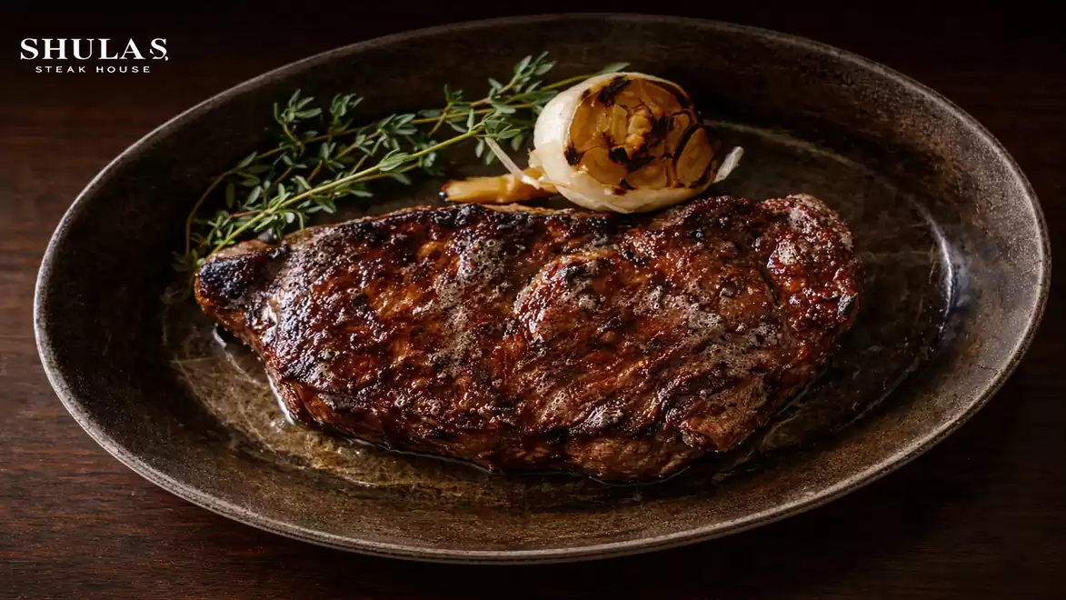 A juicy grilled steak on an oval plate, garnished with a sprig of thyme and a grilled onion slice.