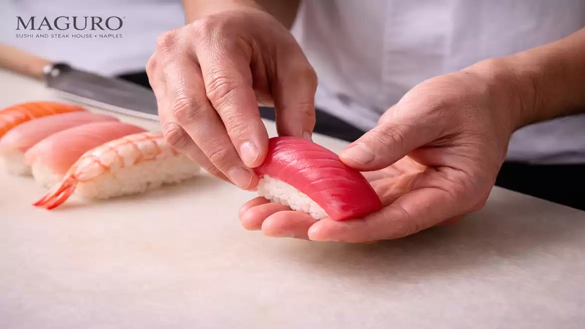 Close-up of a sushi chef preparing nigiri sushi with red and white fish.