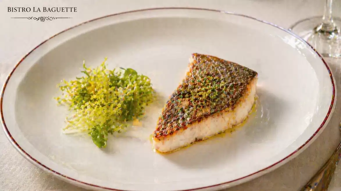 A piece of pan-seared fish with crispy skin served on a white plate with a side of salad at Bistro La Baguette.