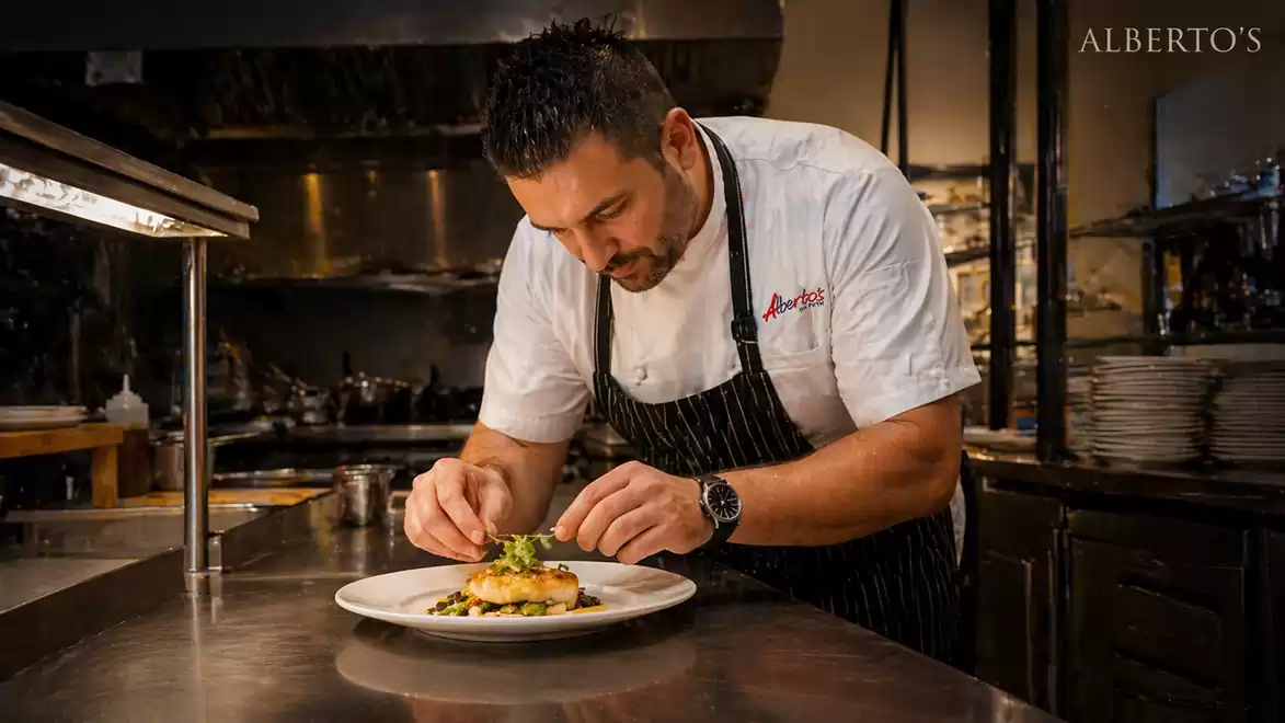 A chef carefully prepares a dish in a professional kitchen. The atmosphere is warm and inviting.