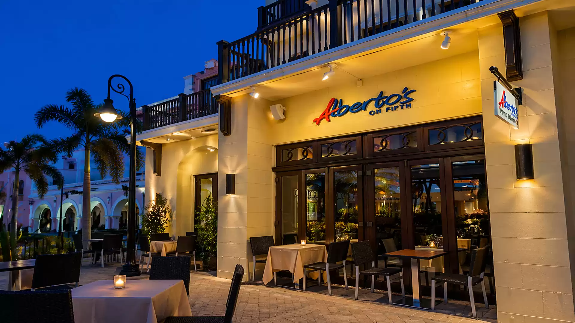 Exterior view of a cozy restaurant at night with table settings on a terrace and warm, inviting lighting.