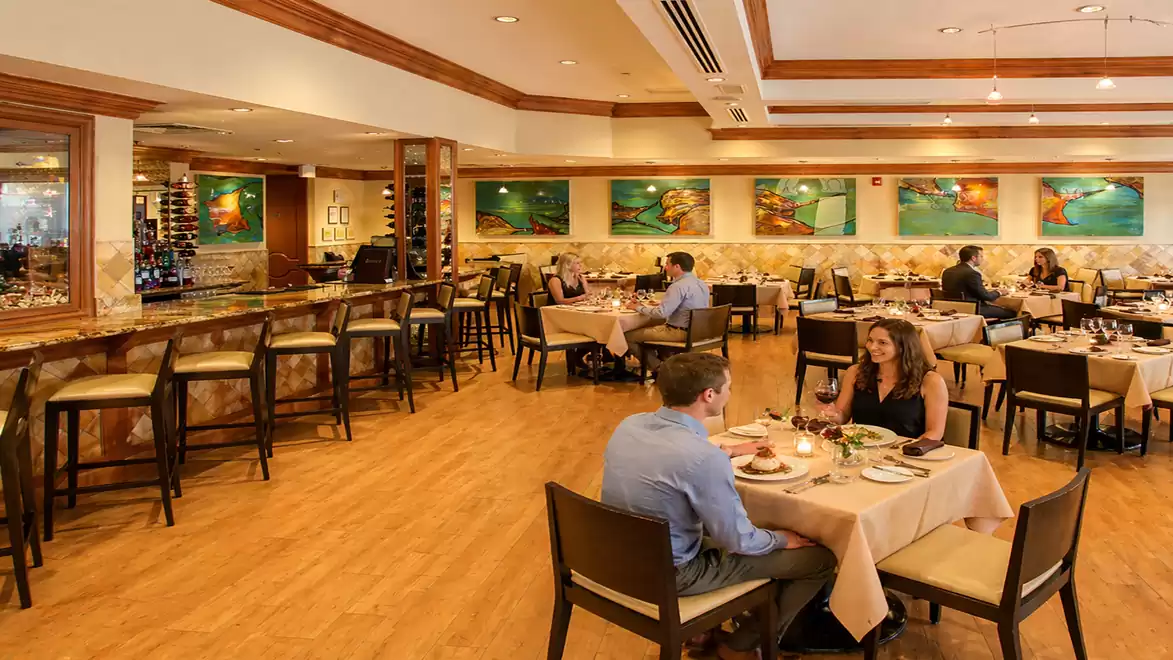 Interior view of an elegant restaurant with patrons at tables and a bar in the background.