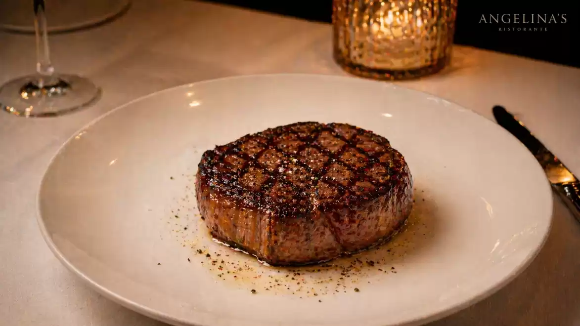 A perfectly grilled steak on a white plate, served in an elegant restaurant setting.