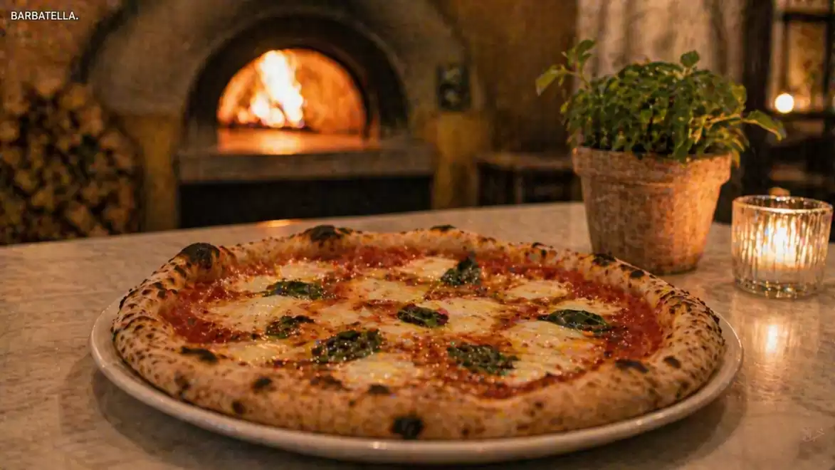 Stone oven pizza with basil in front of a rustic wood-fired oven, next to a plant pot and a candle.