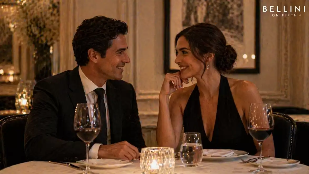 An elegant couple sits in a fine restaurant by candlelight. Both are smiling at each other, enjoying a dinner with wine.