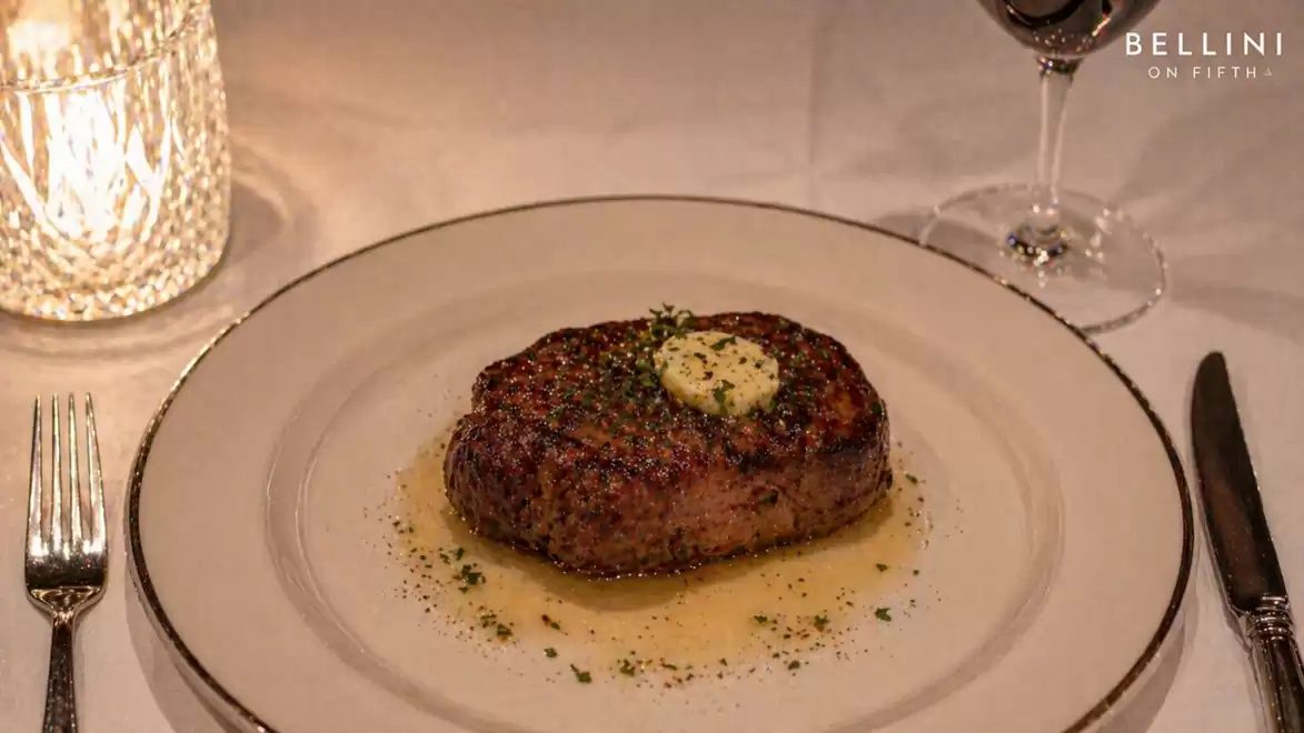 A juicy, perfectly grilled steak with herb butter on an elegant white plate, surrounded by fine cutlery and a glass of red wine in a stylish restaurant.