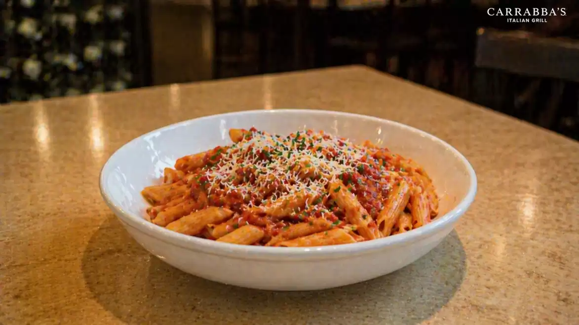 A plate of penne pasta served with tomato sauce and grated cheese on a wooden table in dim lighting
