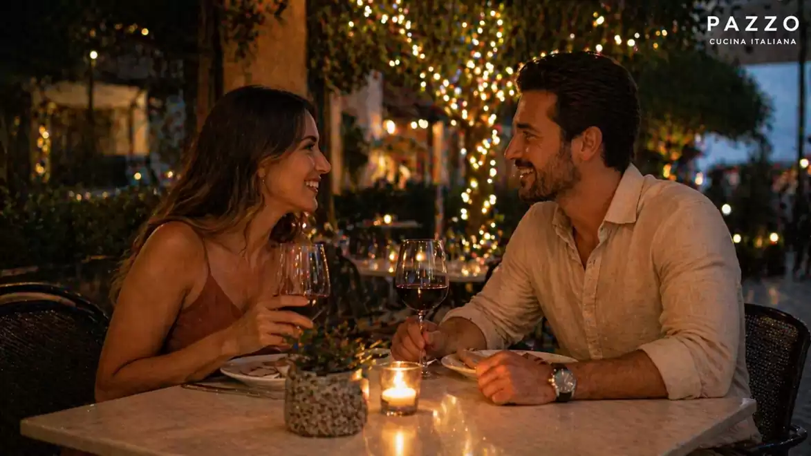 A couple enjoys a romantic candlelit dinner in a restaurant with Italian cuisine. Surrounded by string lights and a cozy atmosphere.