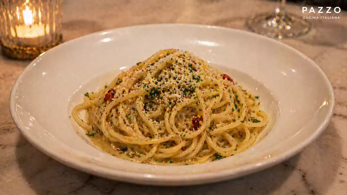 A plate of spaghetti topped with Parmesan cheese and herbs, on a marble table with a candlelight in the background.