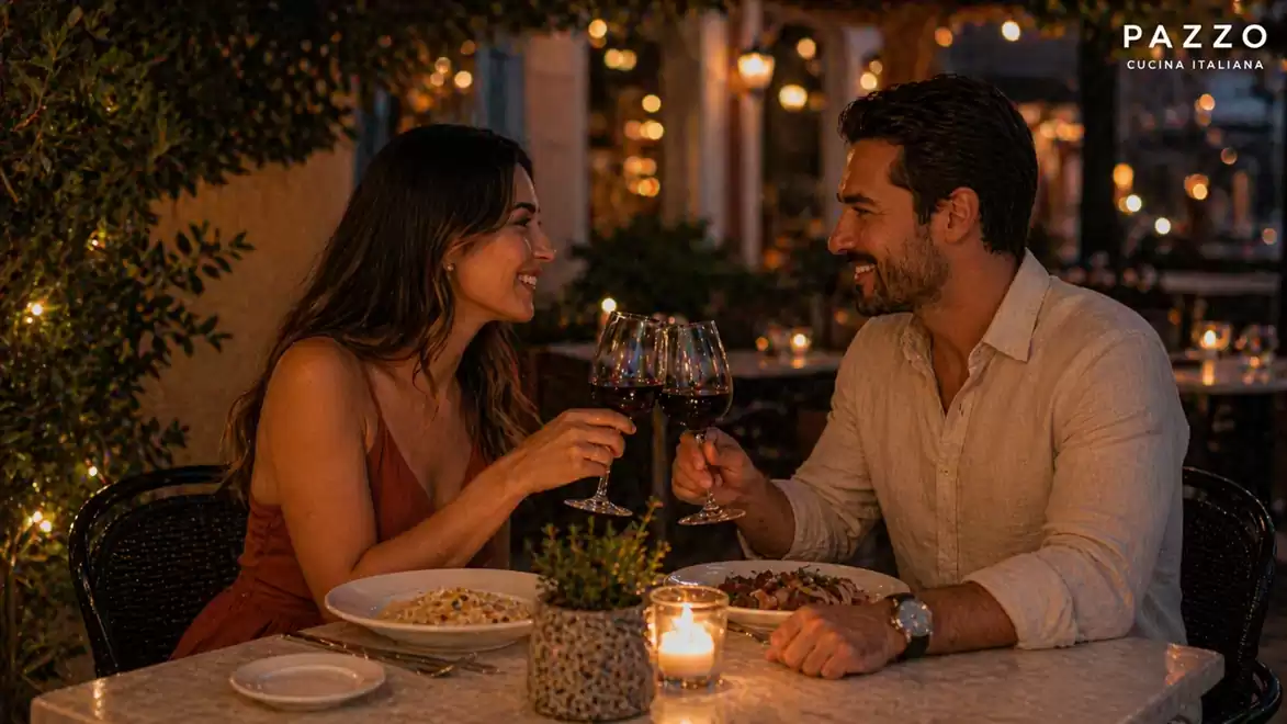 A couple enjoys a romantic outdoor dinner by candlelight, holding two wine glasses.