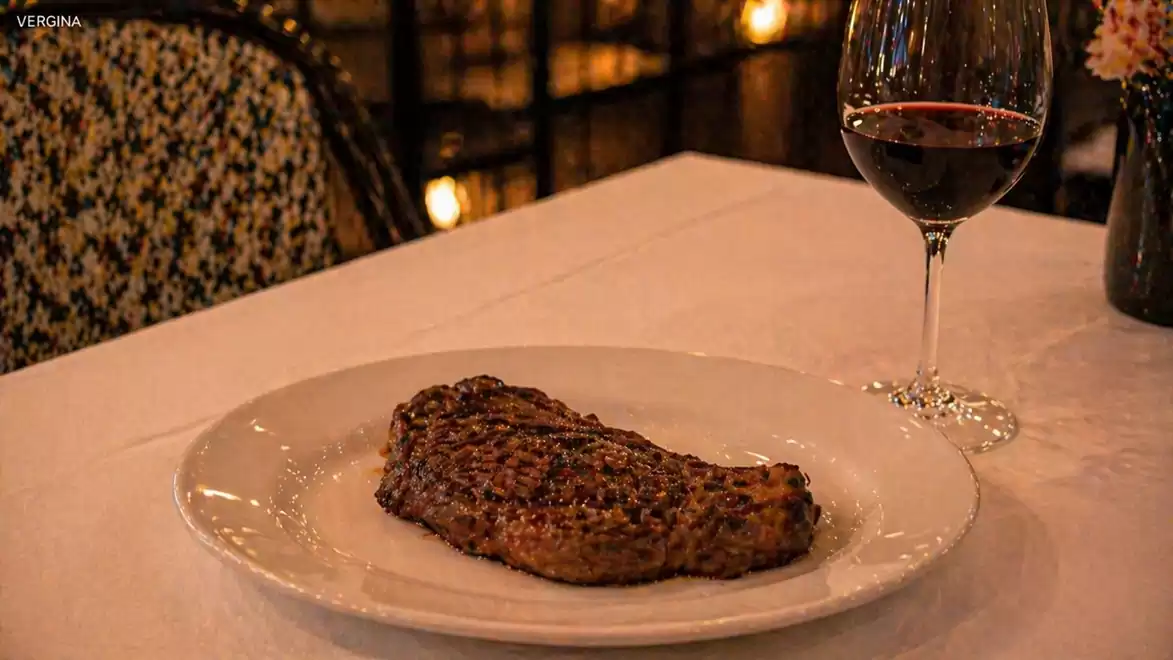 Grilled steak on a white plate with a glass of red wine in an elegant restaurant.