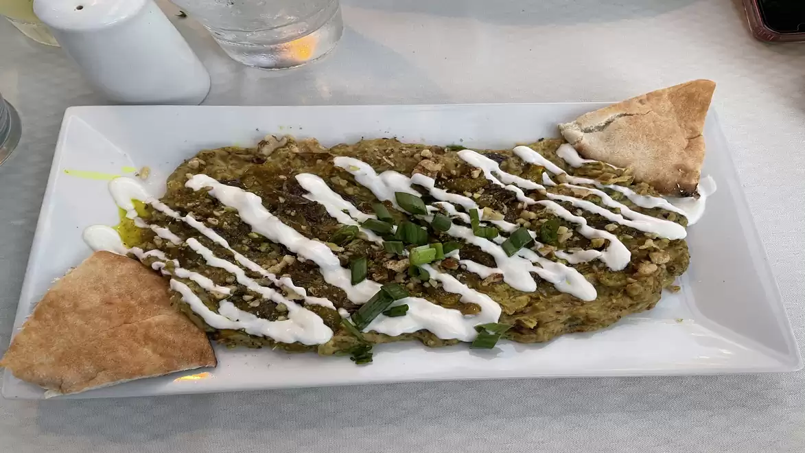 A rectangular plate featuring a serving of Baba Ganoush, garnished with tahini sauce and fresh herbs, accompanied by two pieces of flatbread.