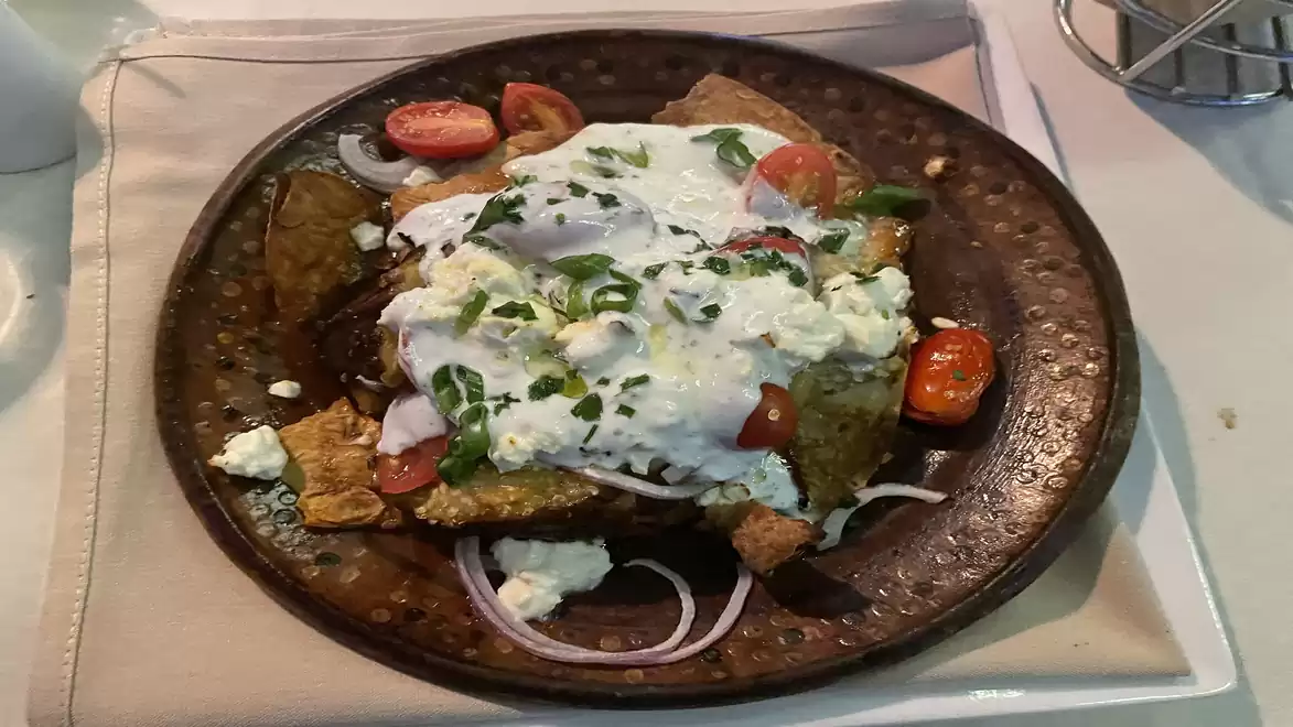 A delicious plate of nachos topped with tomatoes, onions, and cheese, drizzled with yogurt and herbs on a rustic brown plate.