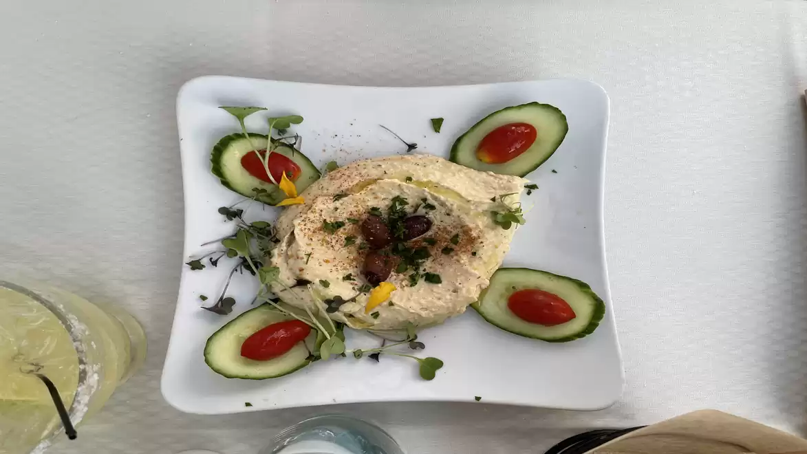 An elegantly presented plate with a cream or mousse in the center, surrounded by thin cucumber slices and halved cherry tomatoes, garnished with fresh herbs on a white plate.