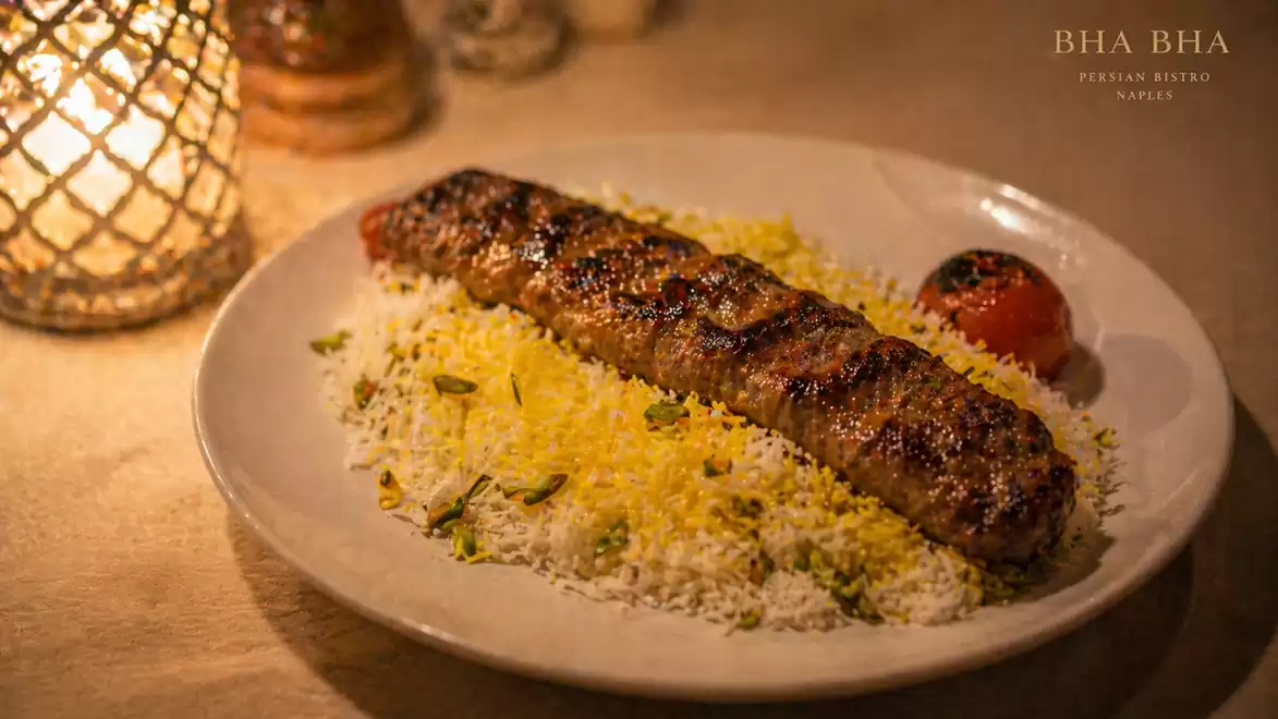 A grilled kebab dish with rice and grilled tomato in ambient lighting.
