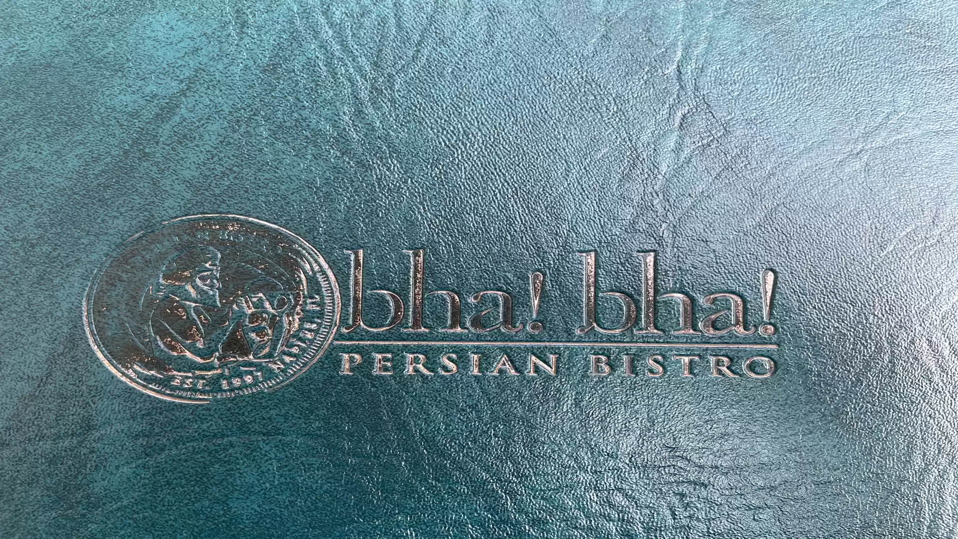 The image shows an embossed logo with the text 'bla! bla! PERSIAN BISTRO' on a textured blue background.