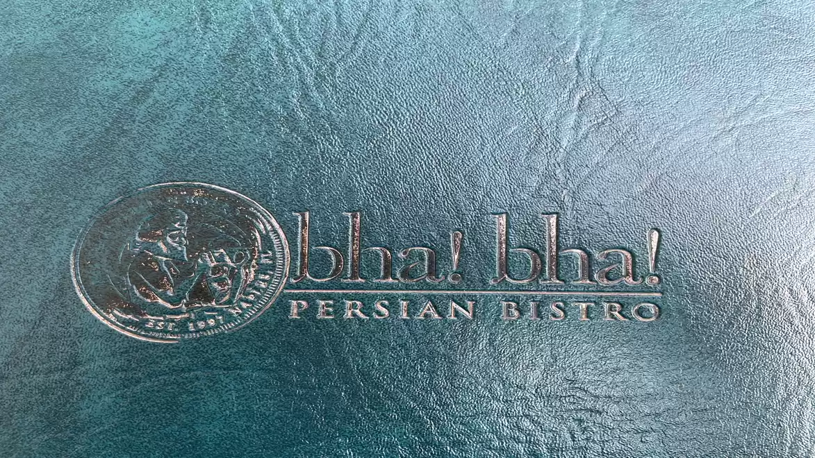 The image shows an embossed logo with the text 'bla! bla! PERSIAN BISTRO' on a textured blue background.