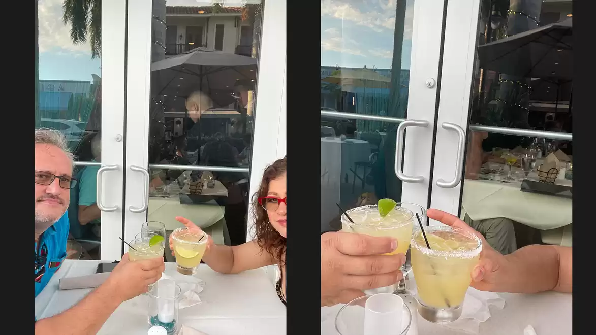 People clinking drinks at a restaurant, a reflective door to the outdoors behind them.