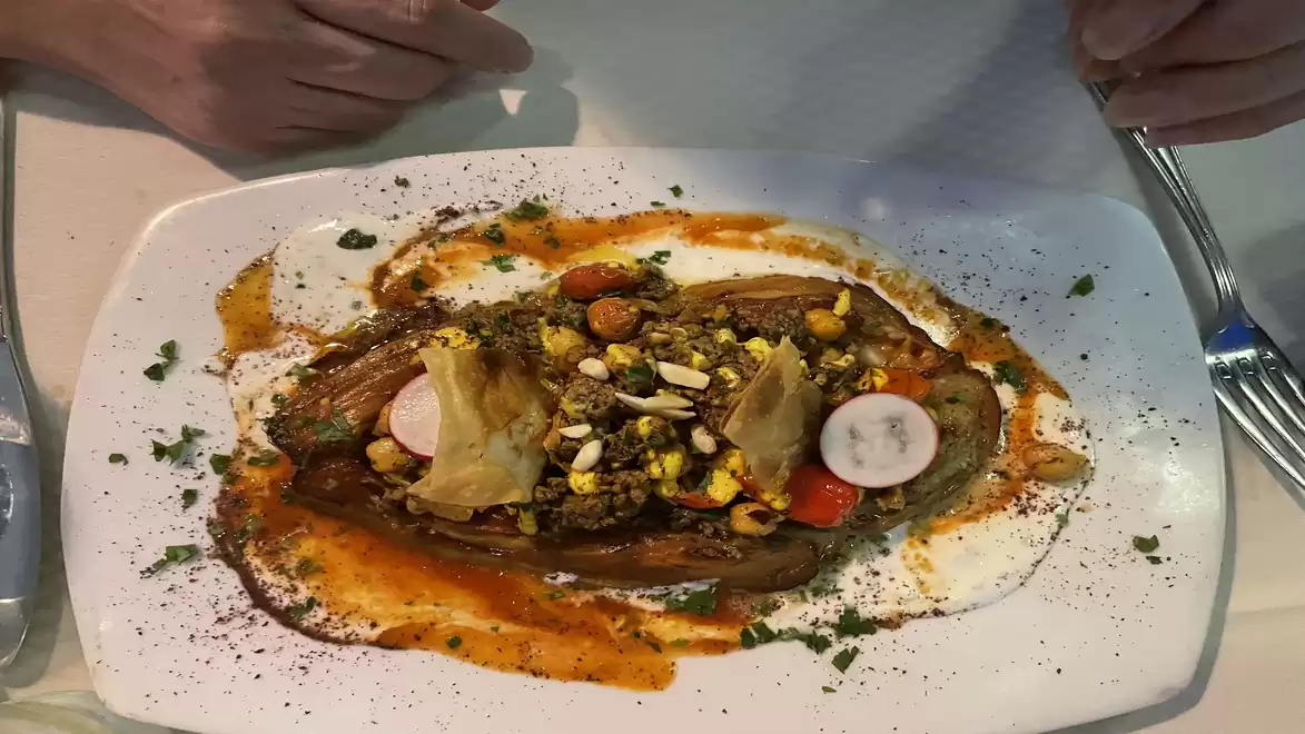A richly decorated dish on a white plate. It features various vegetables and spices, lovingly garnished with sauces and herbs.