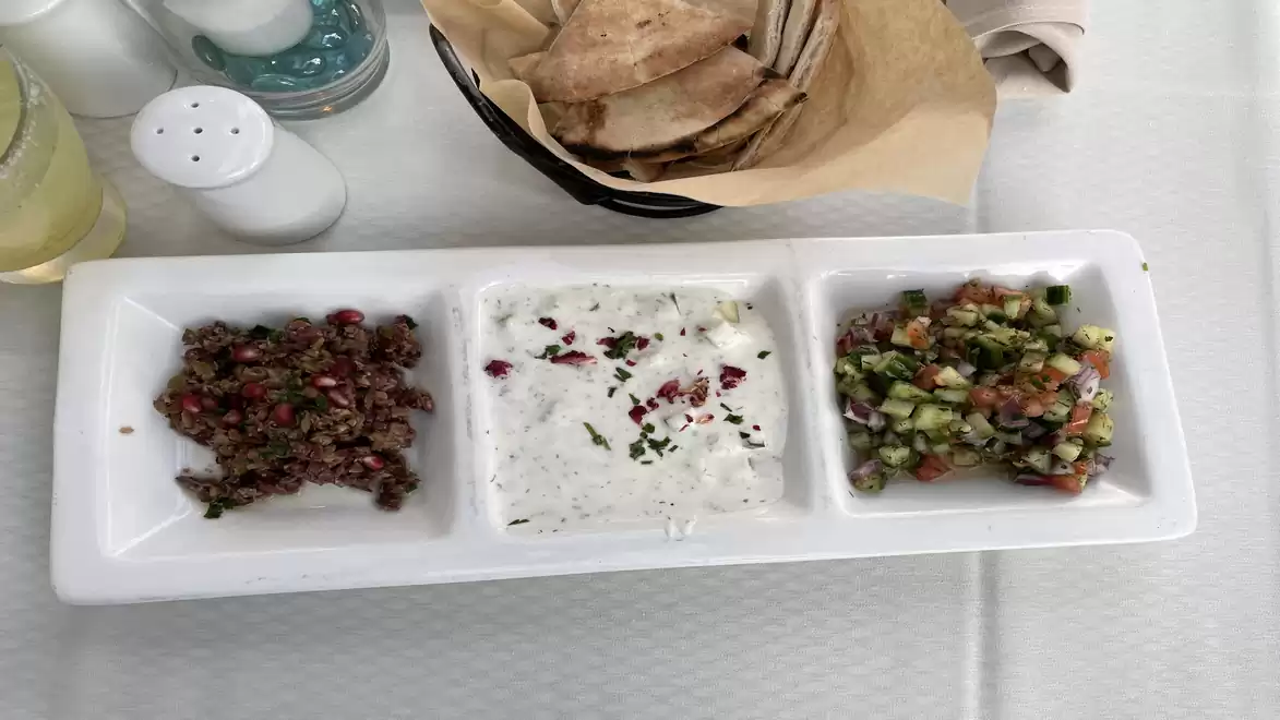 Three bowls with different dips and flatbread on a table.