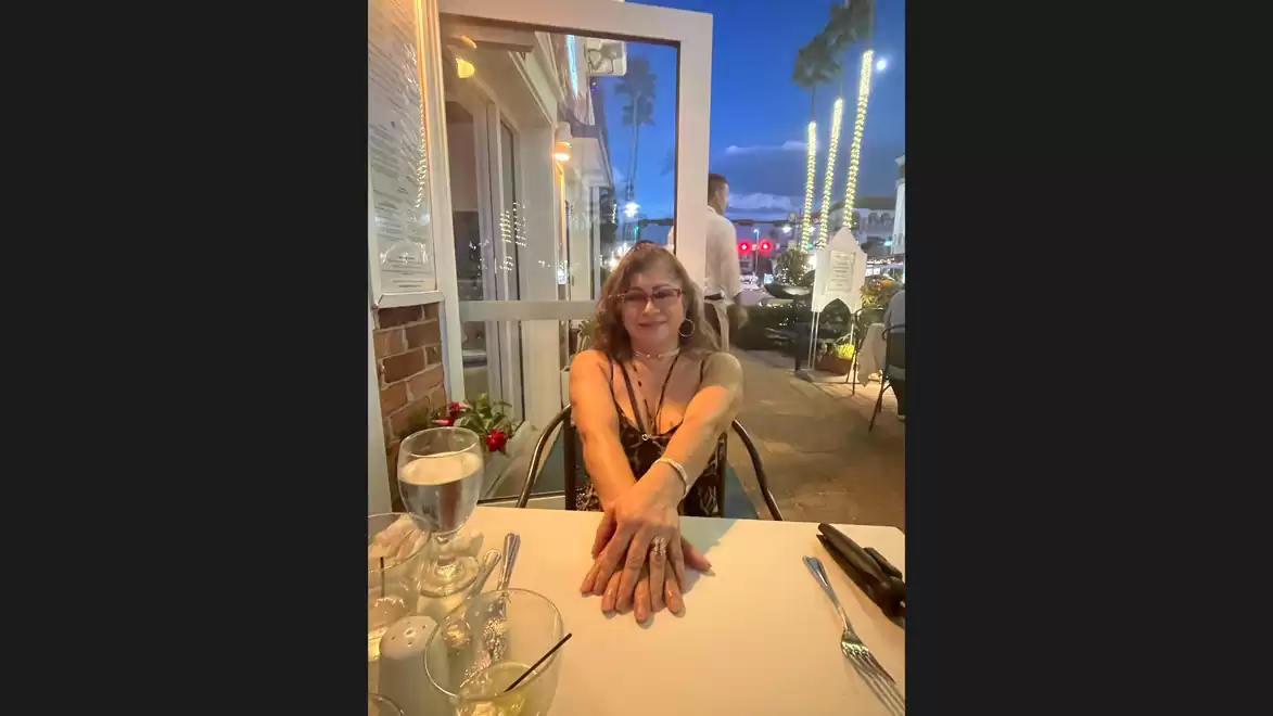 A woman sits at an outdoor restaurant table with drinks as the evening sets in.