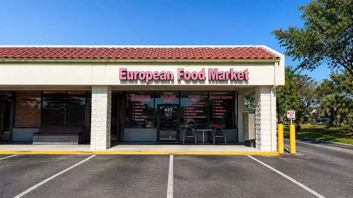 Facade of a store with the sign 'European Food Market' in a shopping center on a sunny day.