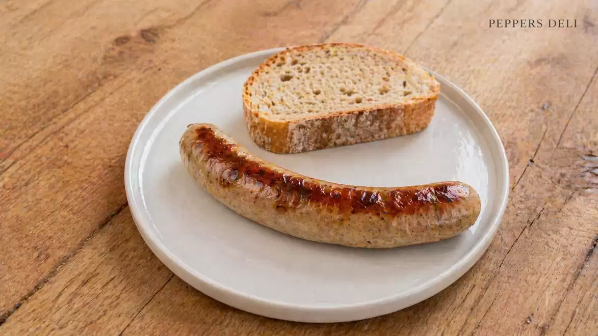 Grilled sausage on a white plate with a slice of bread, served on a wooden table.