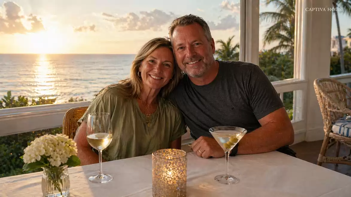 A couple enjoys a romantic sunset by the sea while sitting at a table with cocktails.