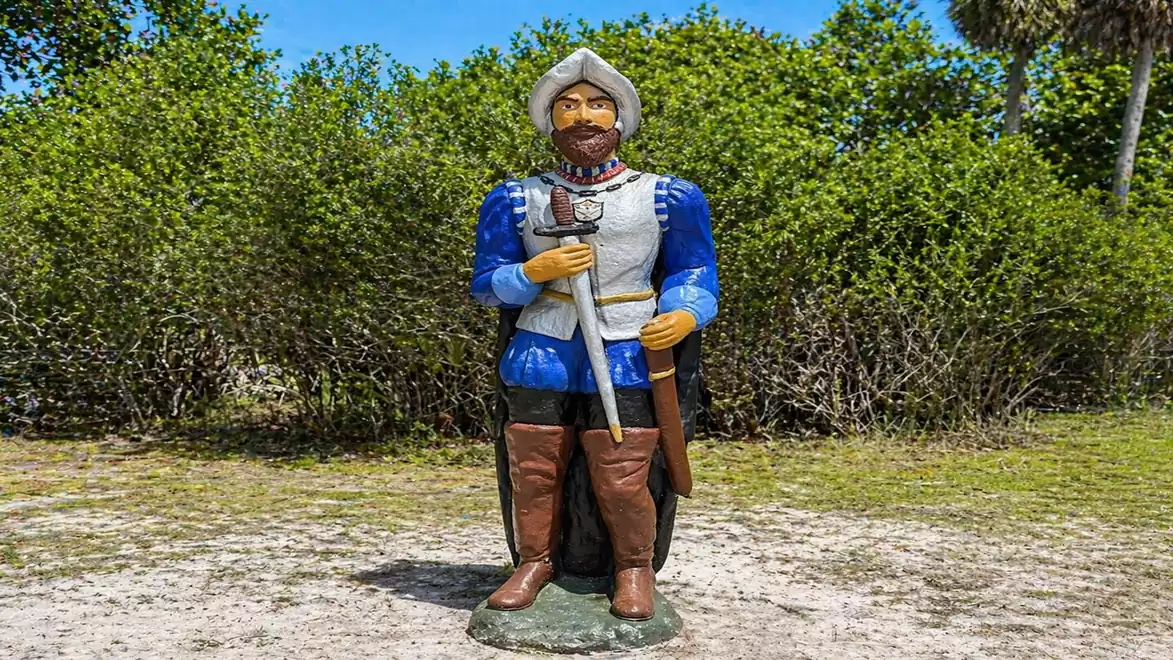 Statue of a historical knight in blue and silver armor standing in a green park.