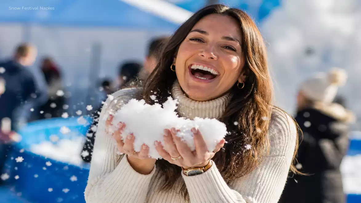 A smiling woman holds snow in her hands at a winter festival.