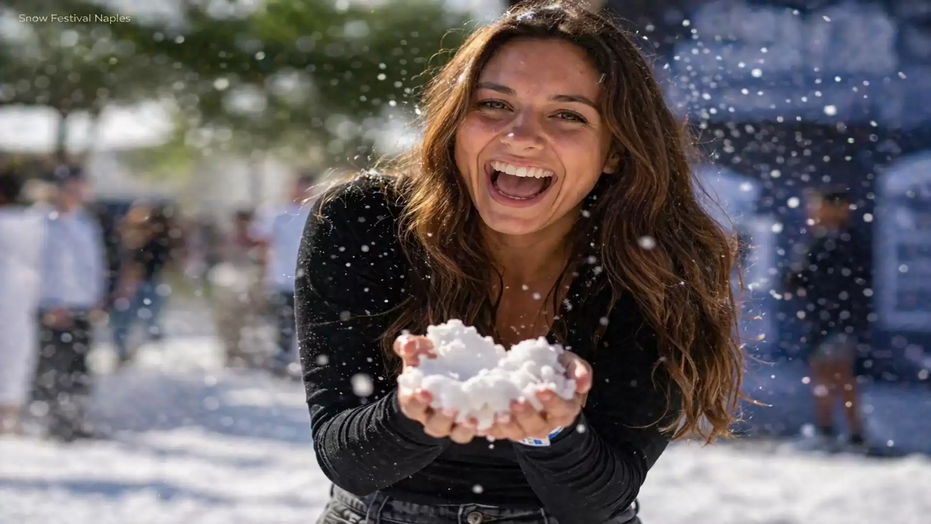 Woman laughing and holding artificial snow in her hands at an outdoor festival.
