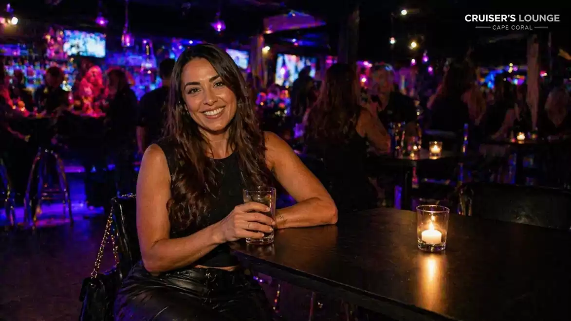 A woman sits in a cozy bar holding a drink. The surroundings are moodily lit.