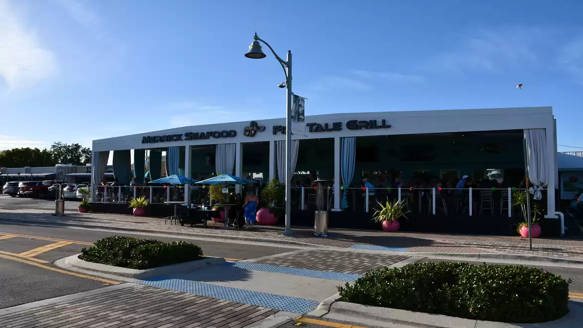 A seaside restaurant with modern architecture, featuring a terrace surrounded by plants and umbrellas, outdoors.