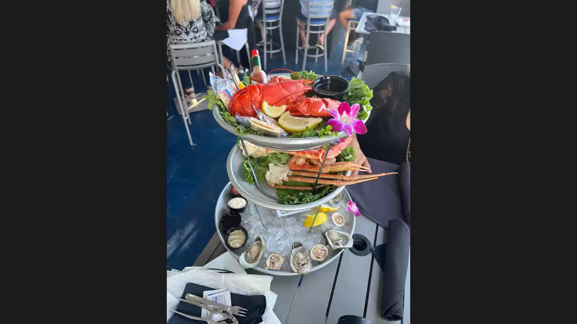 A three-tier seafood platter with lobster, oysters, citrus fruits, and flowers on a table in an elegant restaurant.