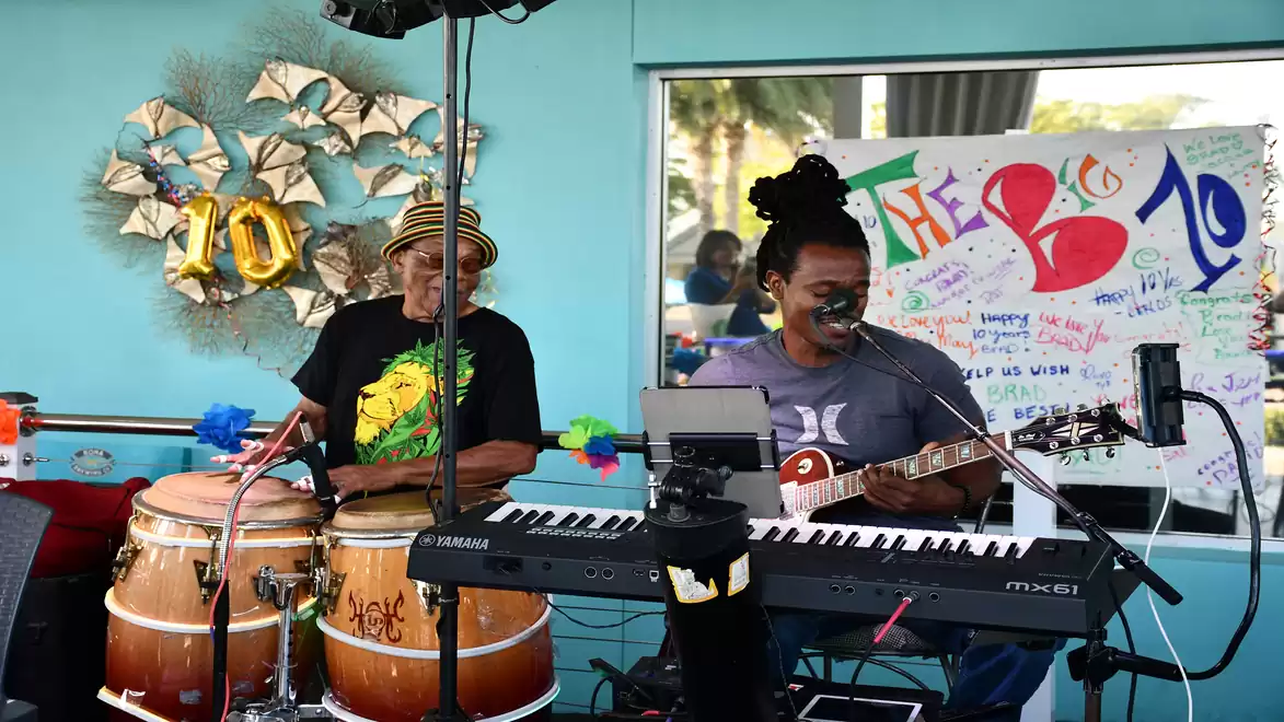 Two musicians playing in a colorful room. One is playing the keyboard, the other the drums.