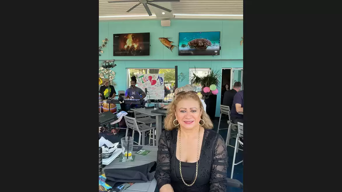 A woman is sitting smiling in a restaurant with a turquoise wall and decorations in the background.