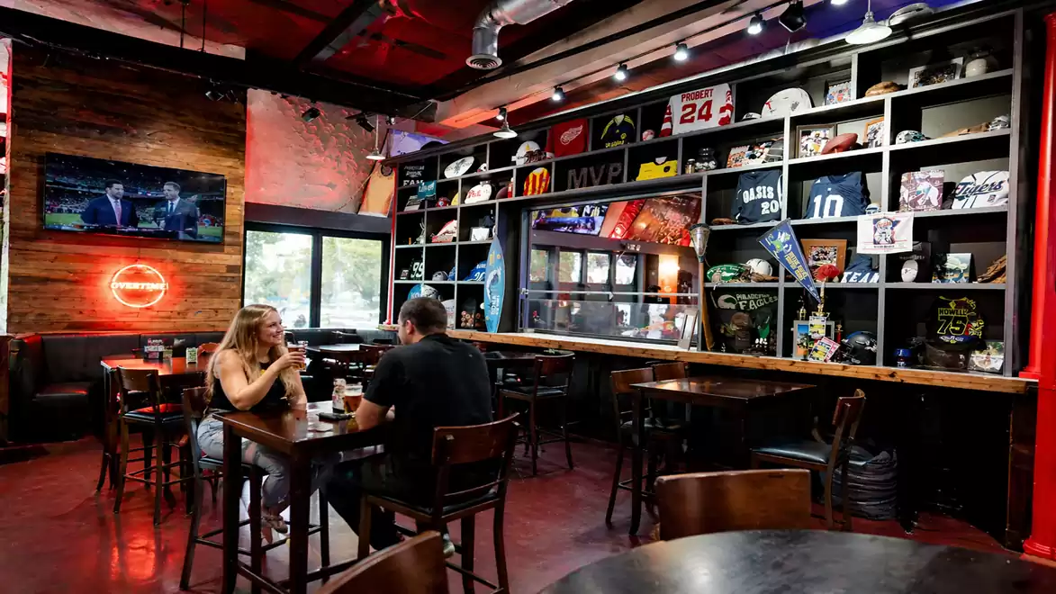 A couple sitting in a cozy sports café surrounded by sports memorabilia and a TV showing a game.